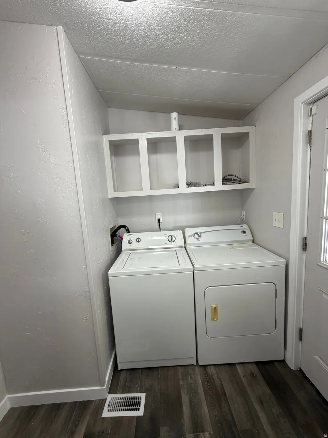 Dedicated laundry area featuring overhead open cabinetry, wood-finish flooring, and a white paneled door