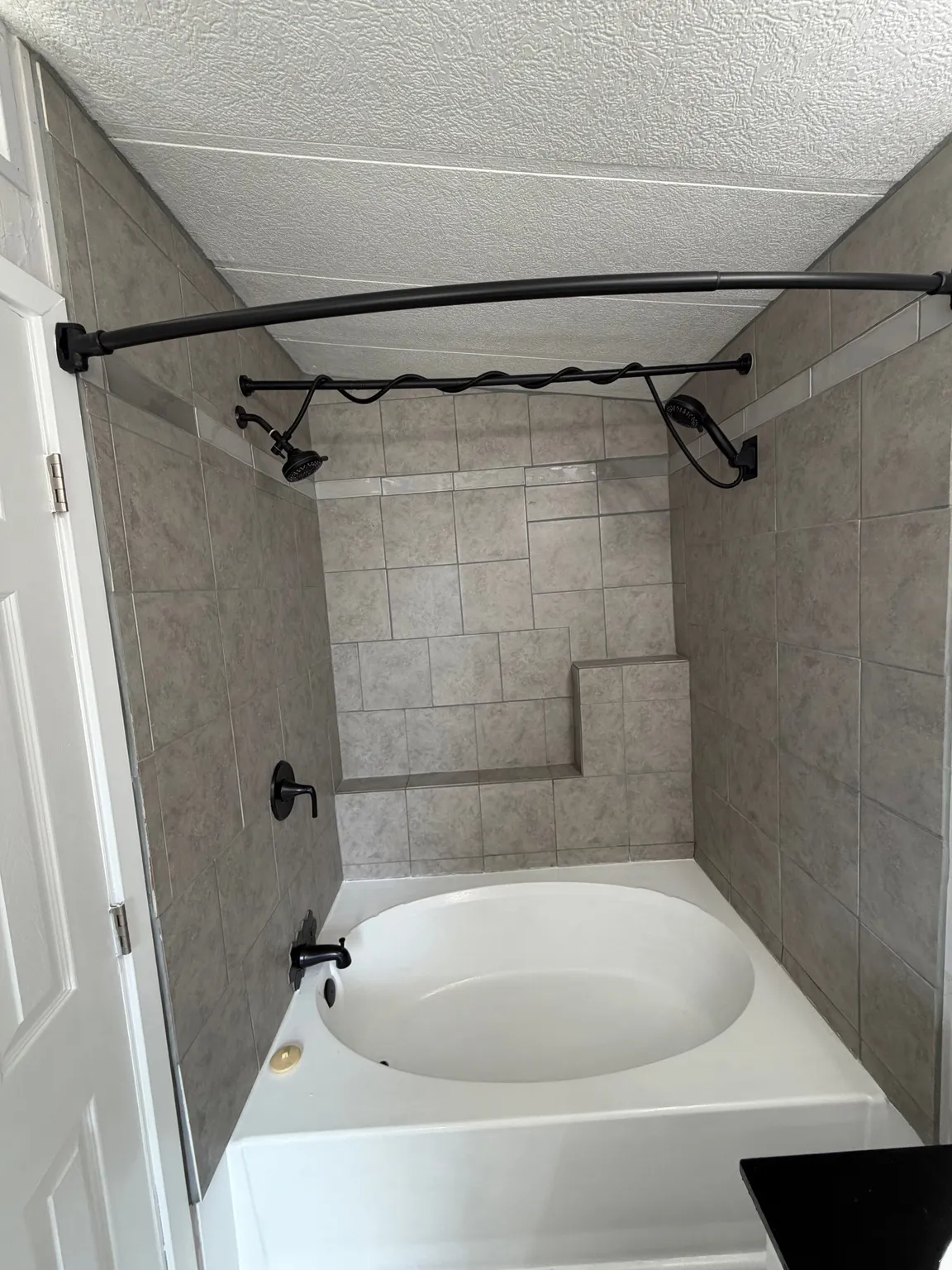 Soaking tub with tiled surround, featuring matte black fixtures, a shower niche, and a curved shower rod