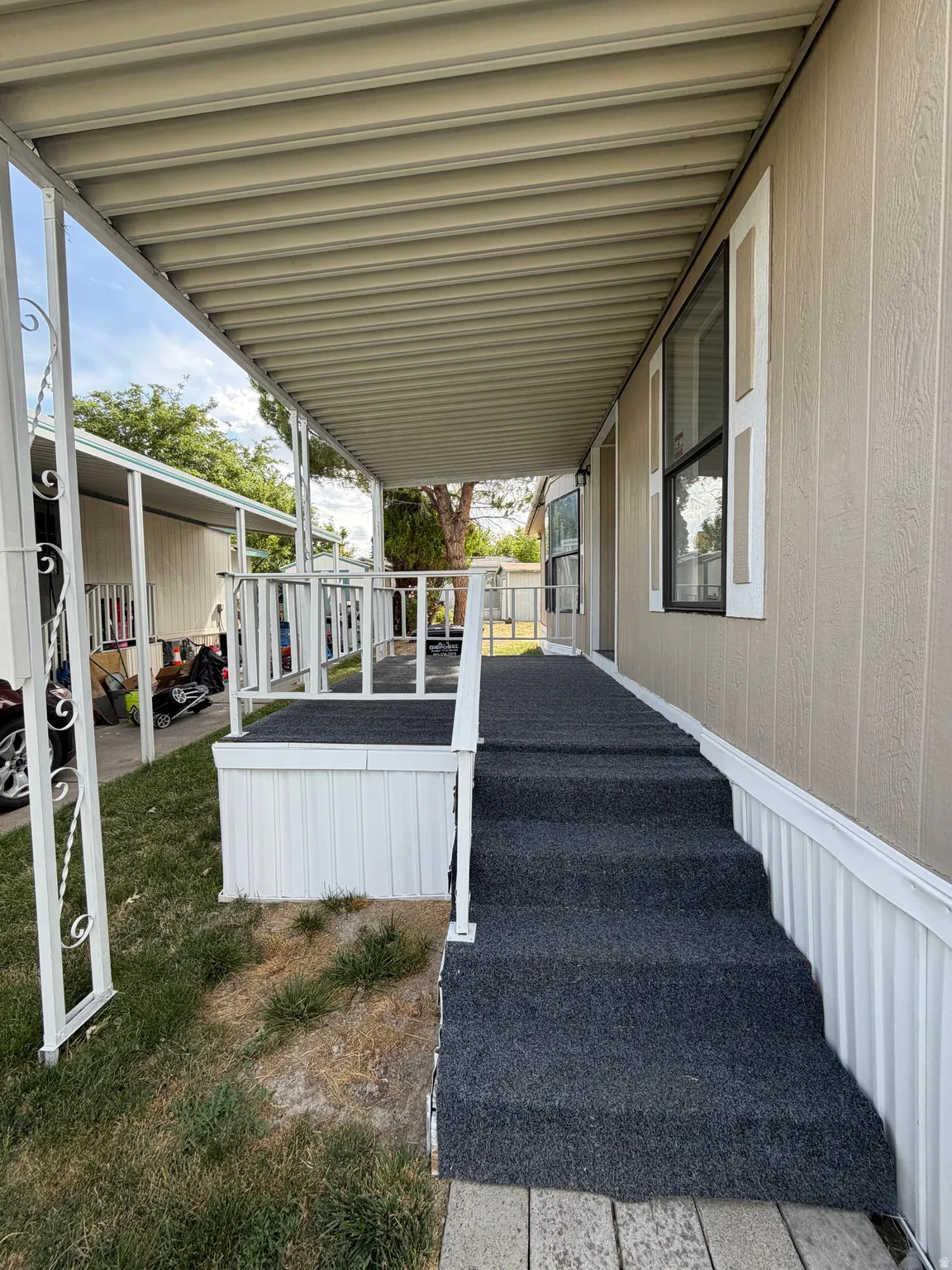 Covered porch with carpeted steps, white railing, and tan siding