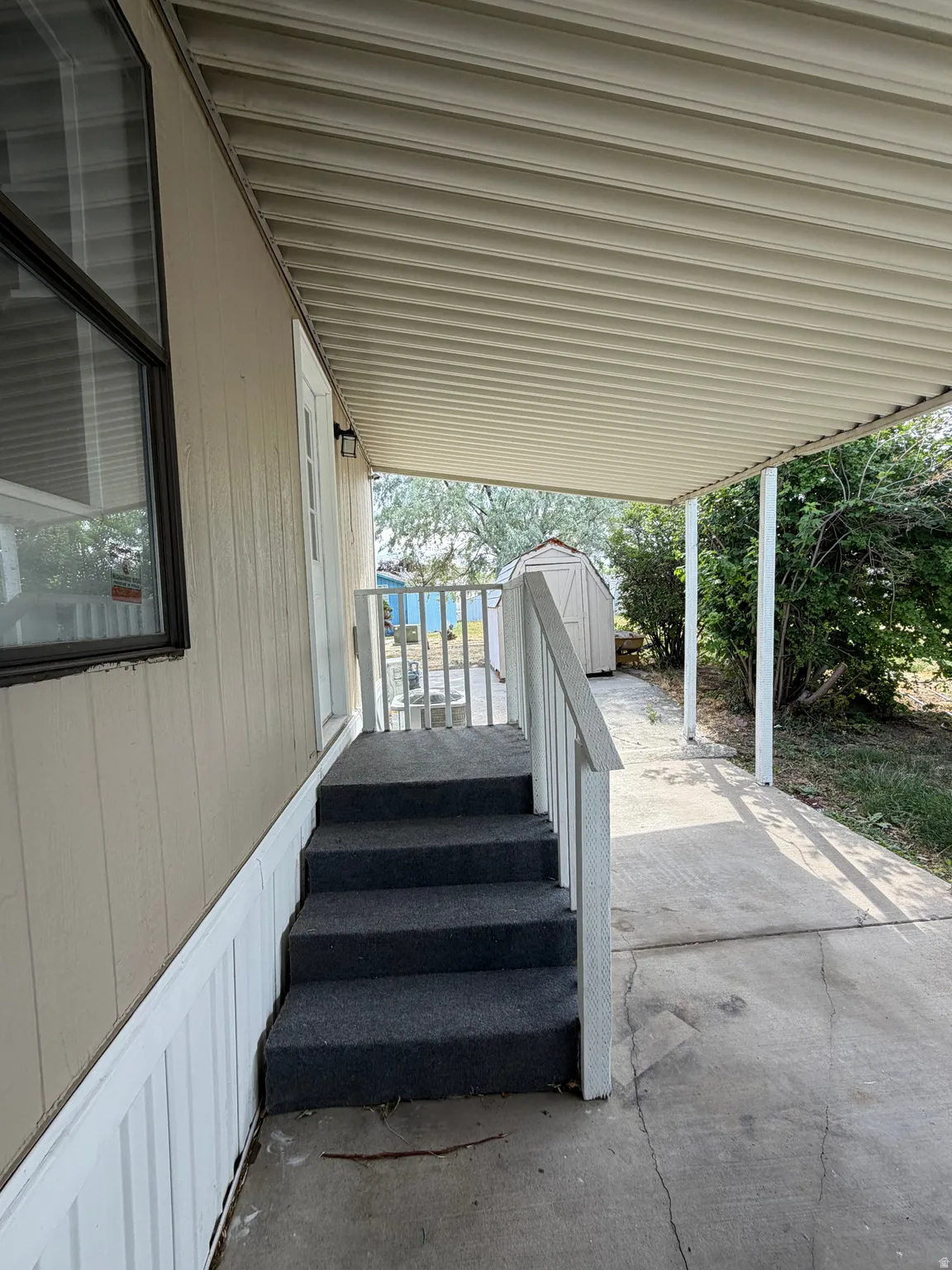 Covered concrete patio with white railing and carpeted steps to entry