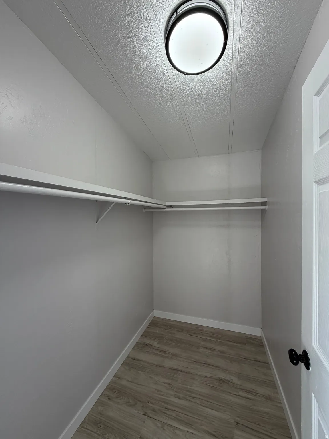 Walk-in closet featuring wood-finish flooring, white baseboards, and a semi-flush mount ceiling light