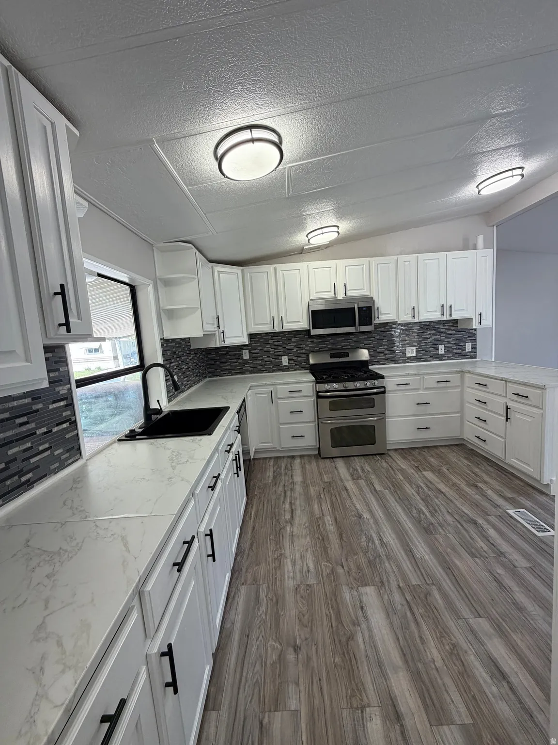 Spacious kitchen featuring white shaker-style cabinetry, stainless steel appliances, and wood-finish flooring