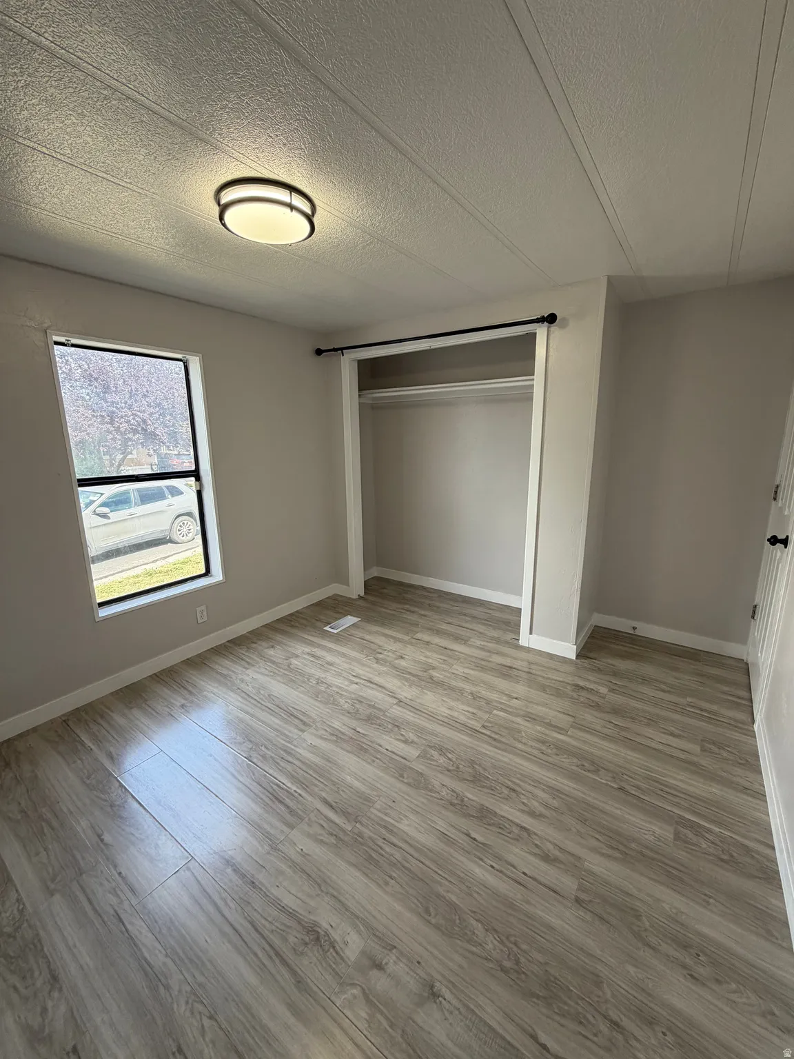Bedroom featuring wood-finish flooring, a contemporary flush-mount ceiling light fixture, a window with exterior visibility, a built-in closet with a hanging rod, and neutral wall paint