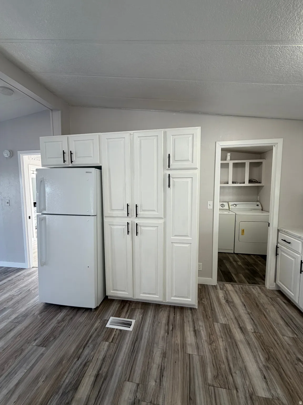 White shaker-style cabinetry with black hardware, wood-finish flooring, and a white refrigerator