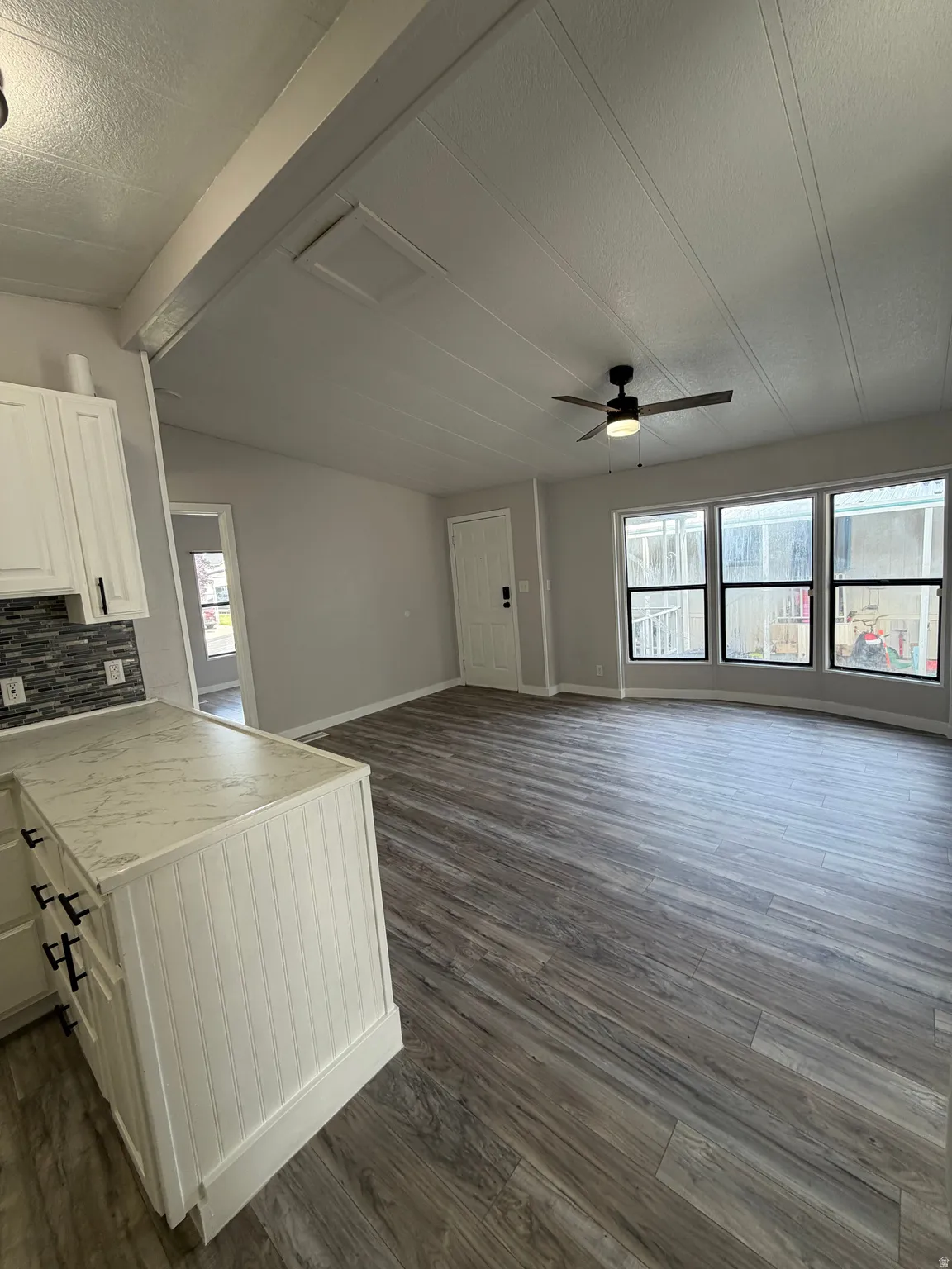 Open-concept living area featuring wood-finish flooring, a contemporary ceiling fan, and a light gray wall palette