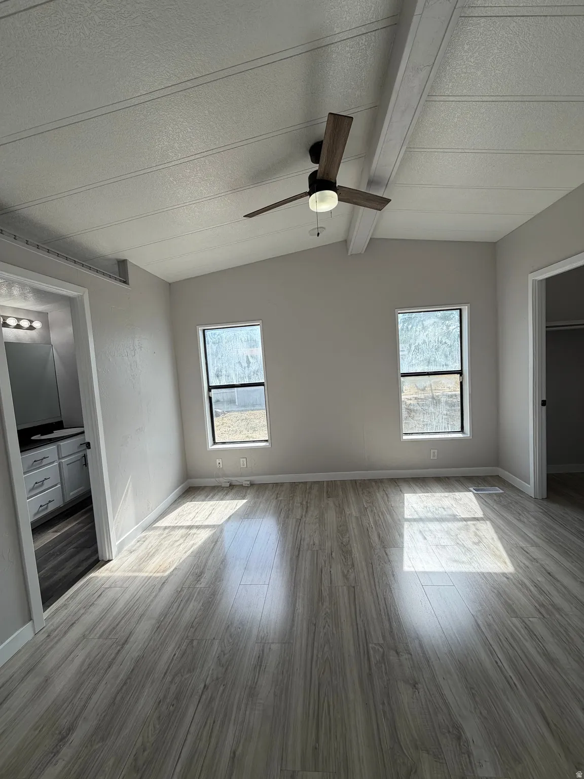 Vaulted ceiling with exposed beams and a modern ceiling fan in a room featuring two windows and wood-finish flooring