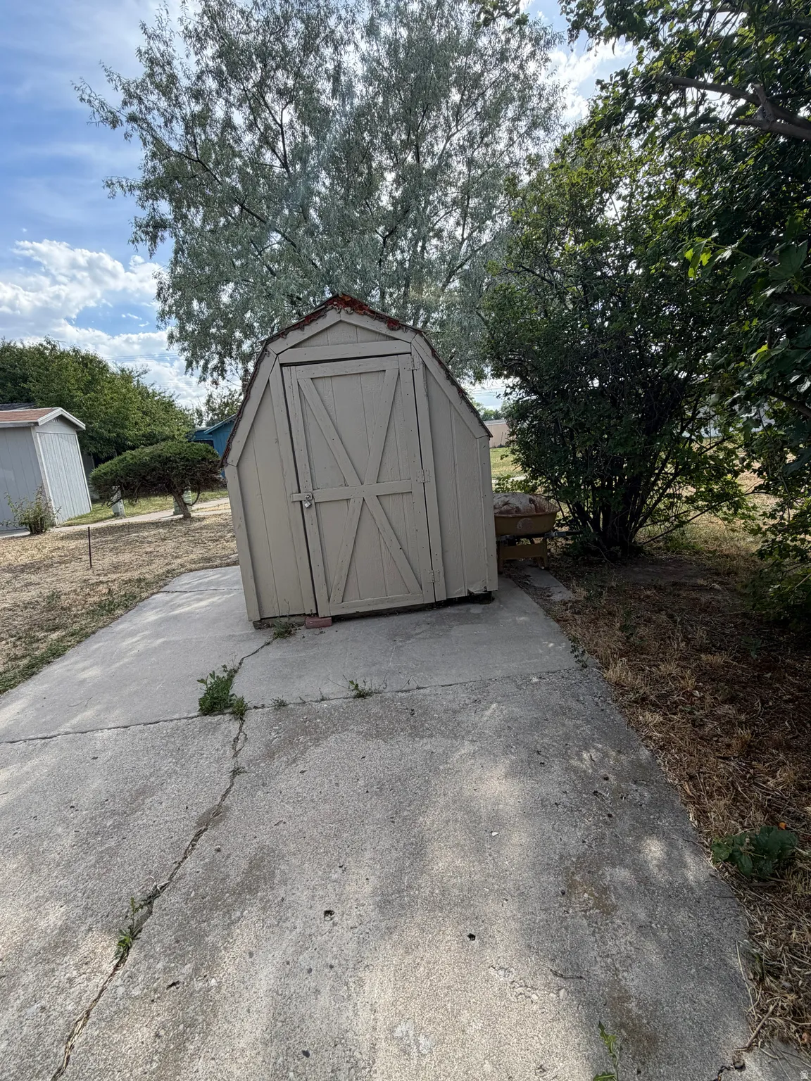 Detached utility shed with a gambrel roof and double barn doors, situated on a concrete pad
