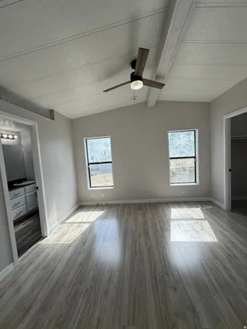 Vaulted ceiling with exposed beams and a modern ceiling fan in a room featuring two windows and wood-finish flooring