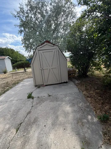 Detached utility shed with a gambrel roof and double barn doors, situated on a concrete pad