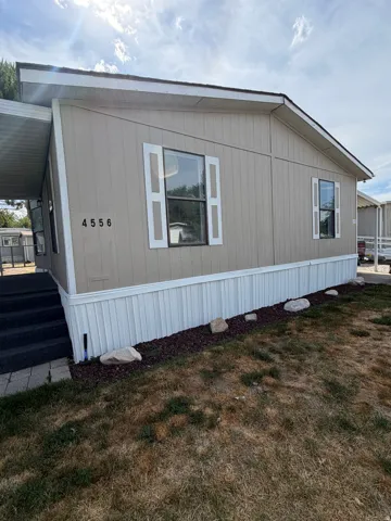 Single-story manufactured home featuring tan siding, white decorative shutters, and a covered porch entry