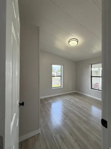 Bright room featuring wood-finish flooring, two windows, a vaulted ceiling, and a modern flush-mount light fixture