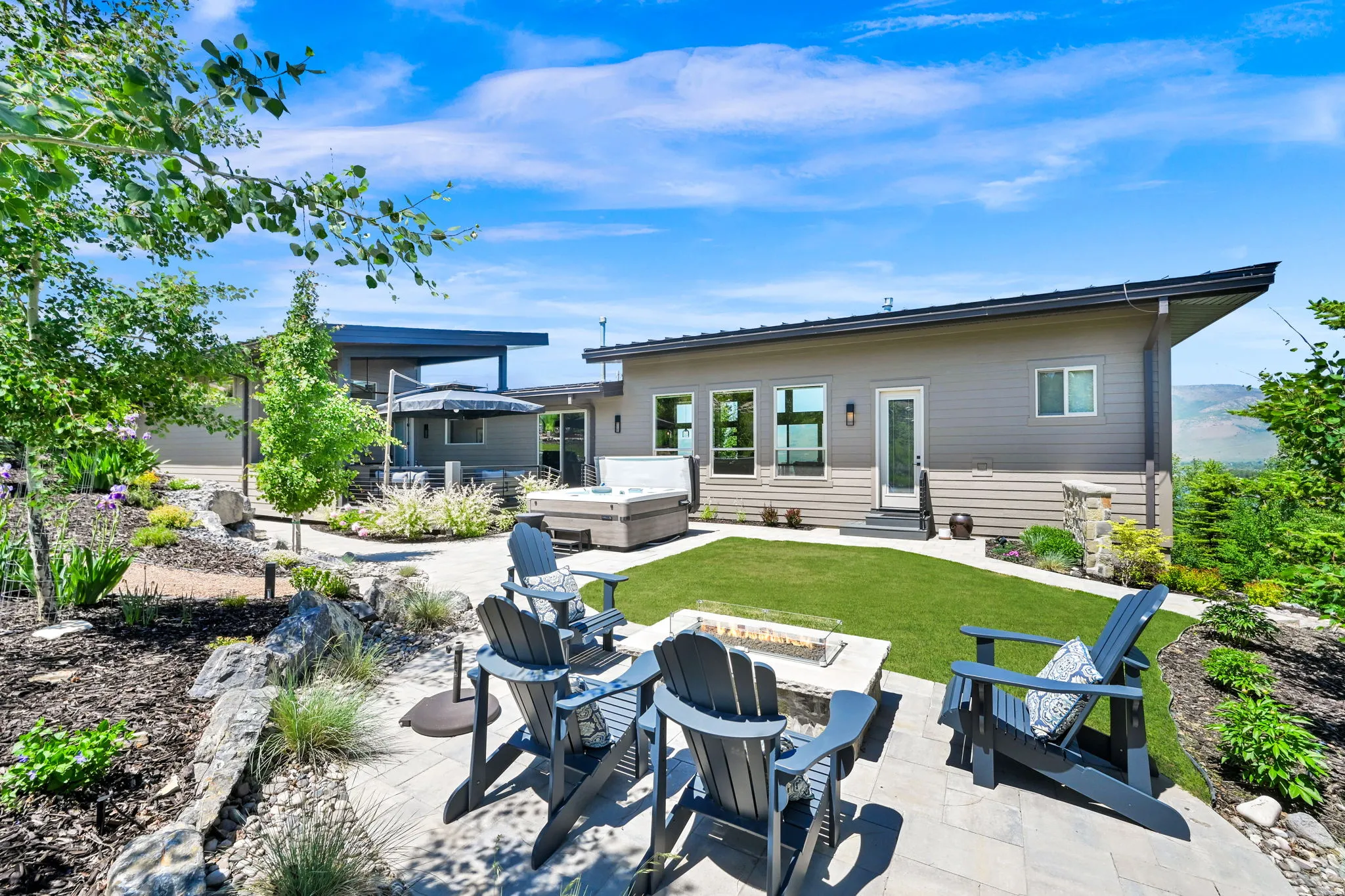 Expansive outdoor living area featuring a paver patio with a built-in fire pit, artificial turf lawn, and a hot tub