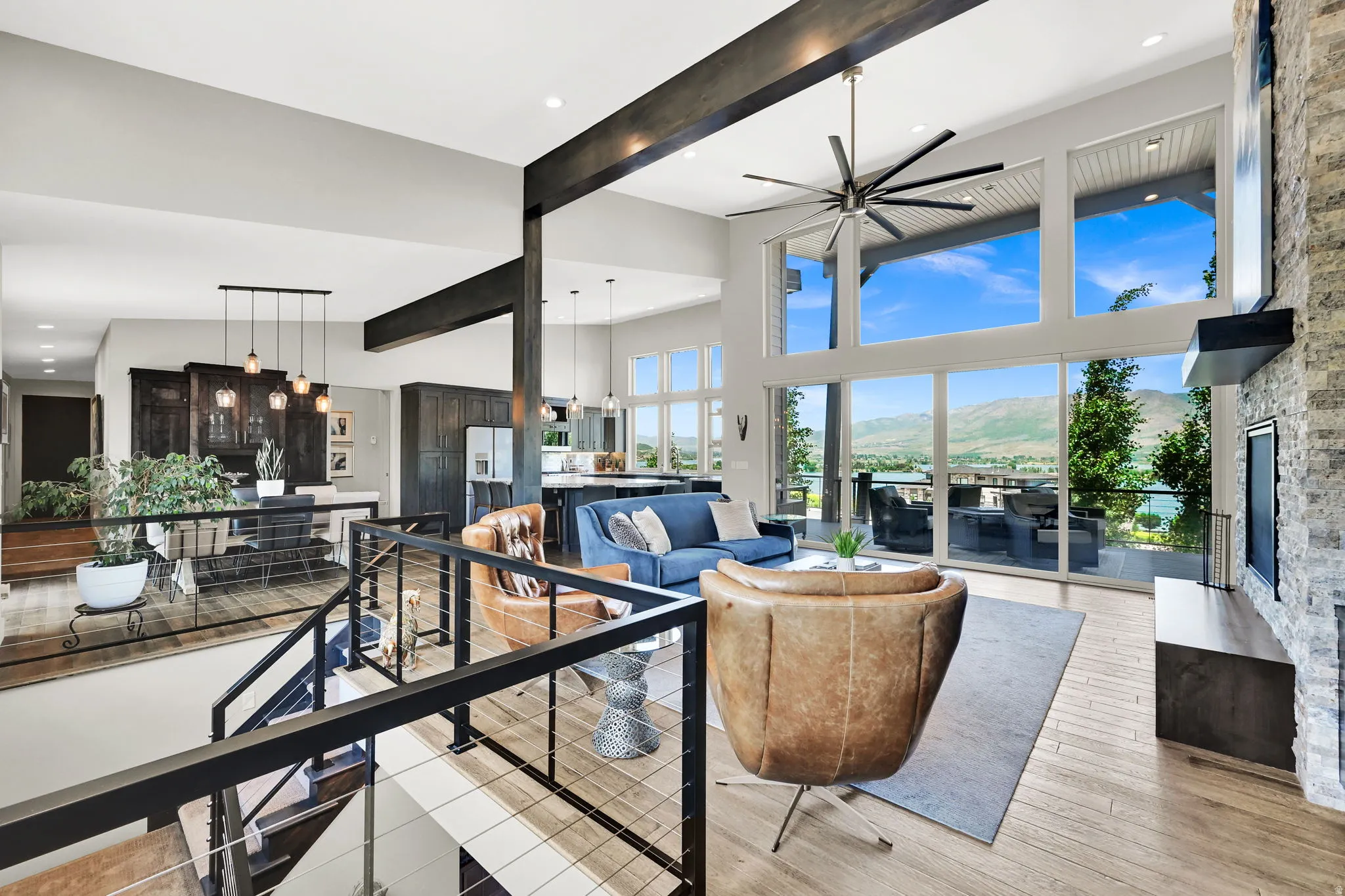 Great room featuring expansive window walls, wood-finish flooring, a stone-clad fireplace, and a large outdoor patio