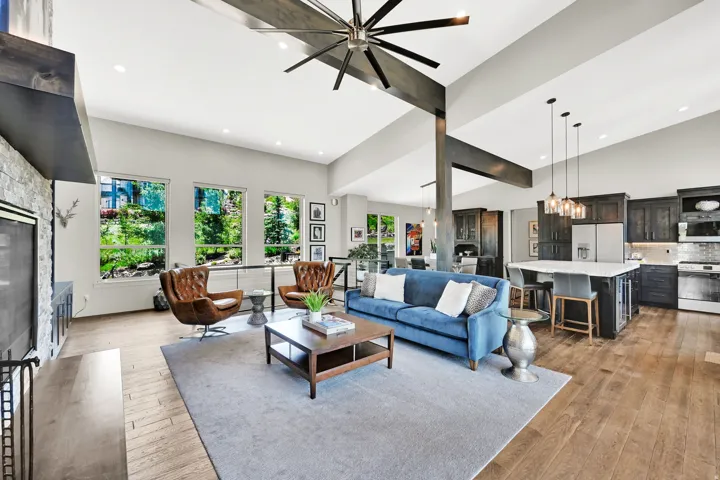 Spacious open-concept living area featuring vaulted ceilings, wood-finish flooring, a stone-front fireplace, and large windows