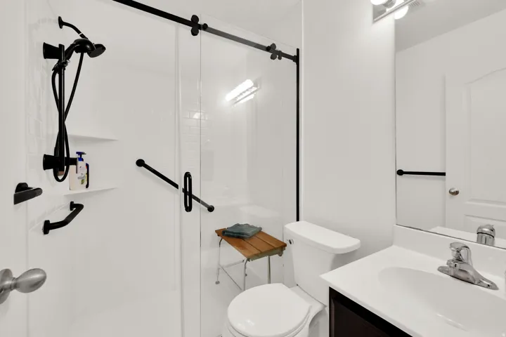 Updated hall bathroom featuring a glass-enclosed shower with matte black fixtures and beautiful new tile floors.