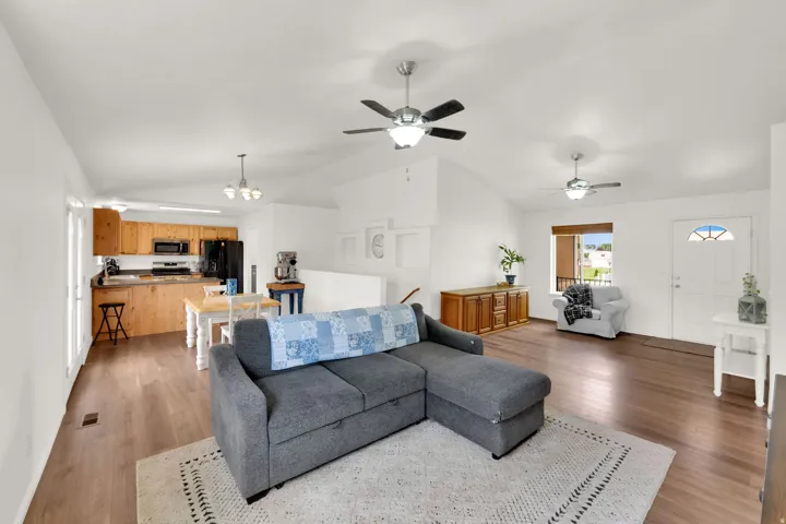 Spacious open-concept interior featuring vaulted ceilings, wood-finish flooring, and view of the kitchen.