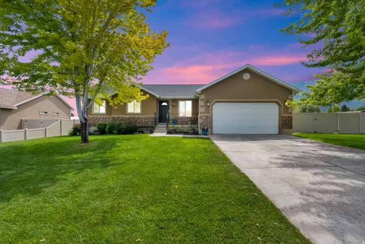 Stucco and stone facade home featuring a two-car garage, concrete driveway, and front lawn with mature trees
