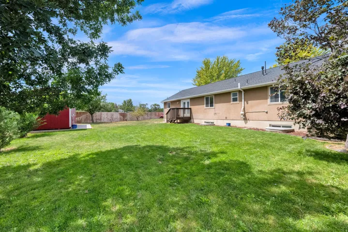 Expansive grassy back yard featuring a red storage shed, mature trees, wood privacy fencing, and a rear deck with direct access to the residence