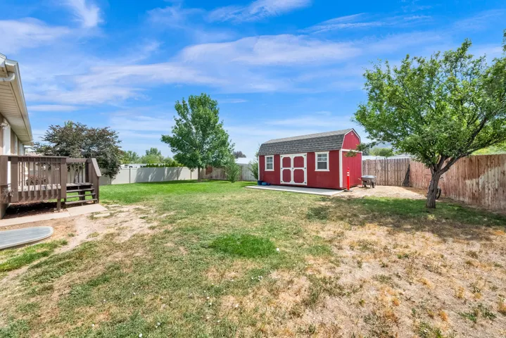 Expansive backyard featuring a red gambrel roof shed with white trim, a brown wood deck with railings and steps, and a partial wood privacy fence
