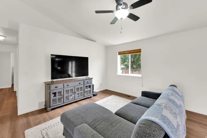 Living area featuring wood-finish flooring, vaulted ceiling, and a ceiling fan with integrated lighting