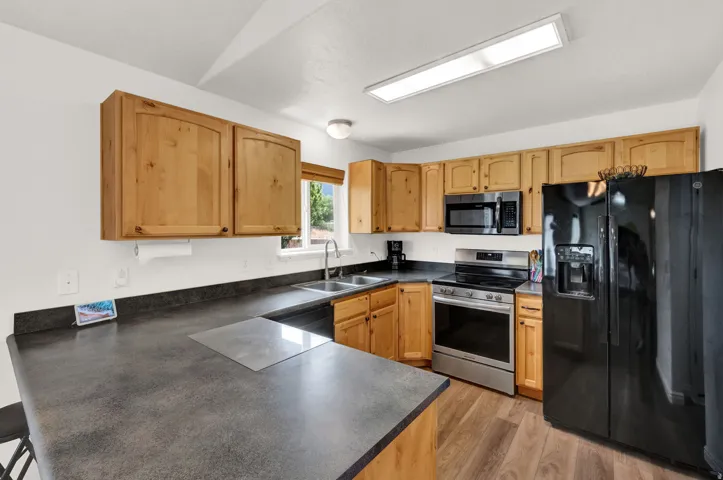 Kitchen featuring wood cabinetry, black countertops, stainless steel appliances, and wood-finish flooring
