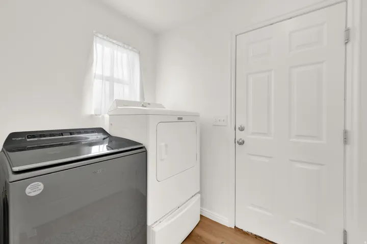 Dedicated laundry area with a window, white walls, and wood-finish flooring