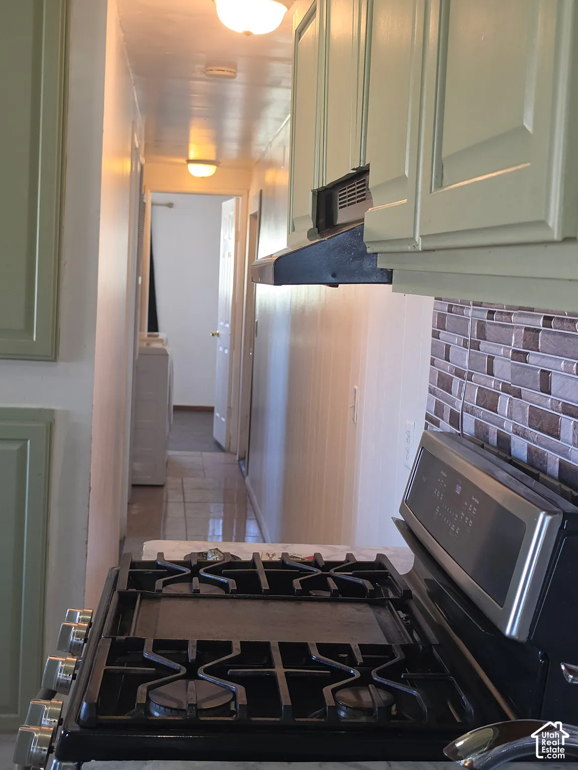 Integrated range with cooktop, mosaic tile backsplash, light-toned upper cabinetry, and overhead range hood