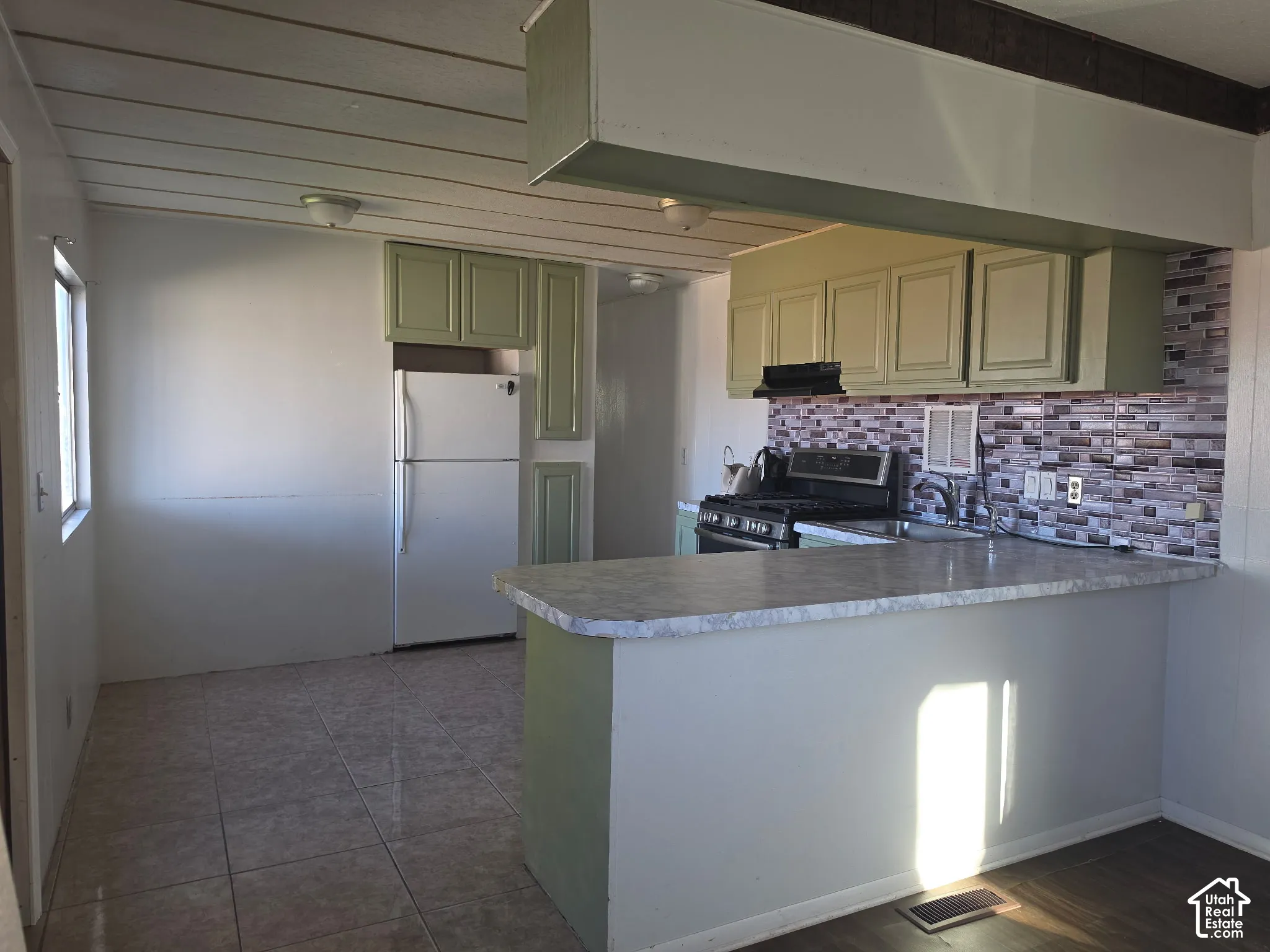 Kitchen featuring light green cabinetry, tile backsplash, and an integrated breakfast bar