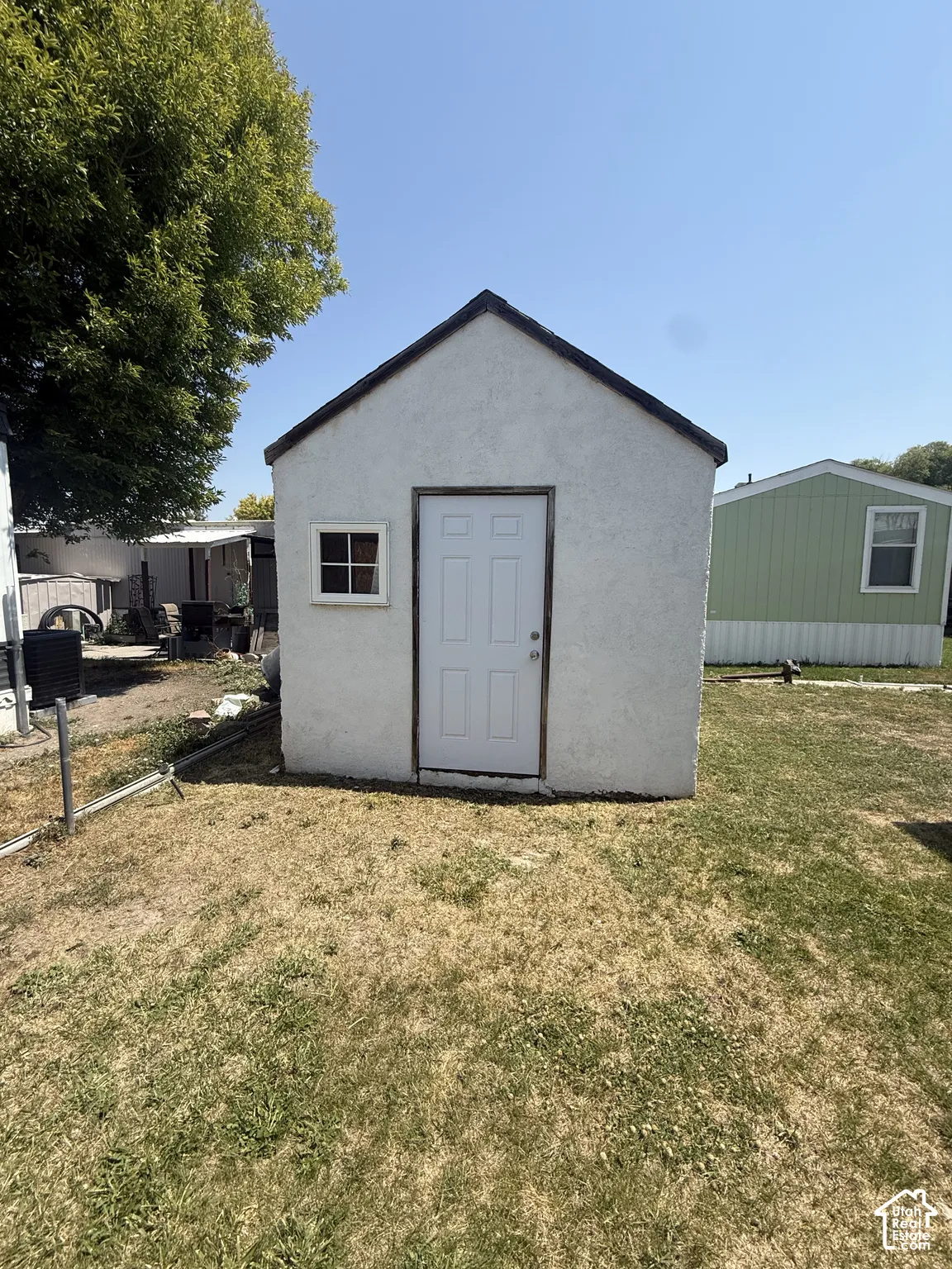 Charming storage shed featuring a peaked roof with dark trim, single-pane window, and white entry door