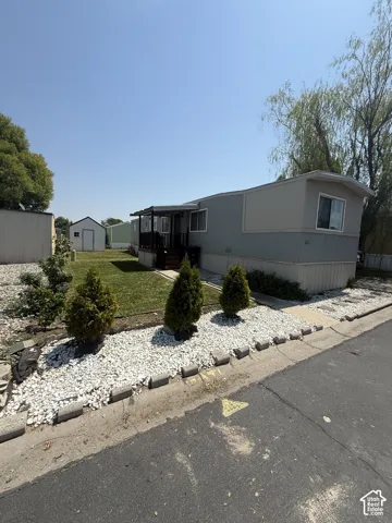 Charming manufactured home featuring a manicured front landscape with mature evergreen plantings, white gravel hardscaping, and defined border edging