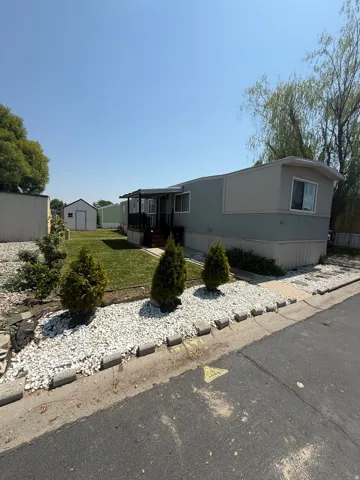 Charming manufactured home featuring a manicured front landscape with mature evergreen plantings, white gravel hardscaping, and defined border edging