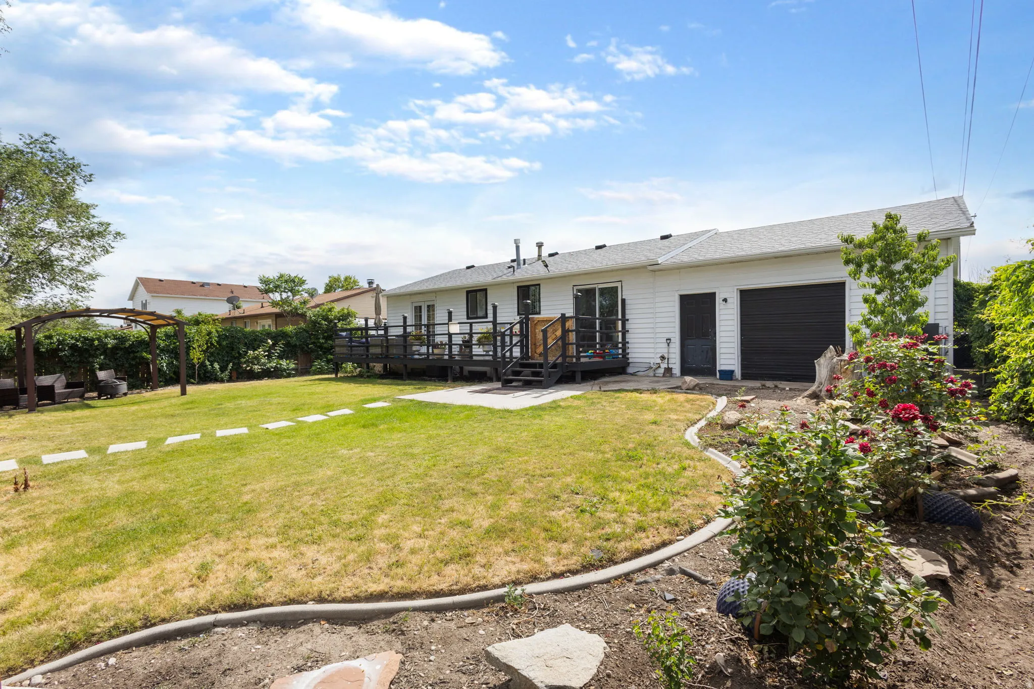 Expansive backyard featuring a manicured lawn with stepping stones, a pergola, and a multi-level deck