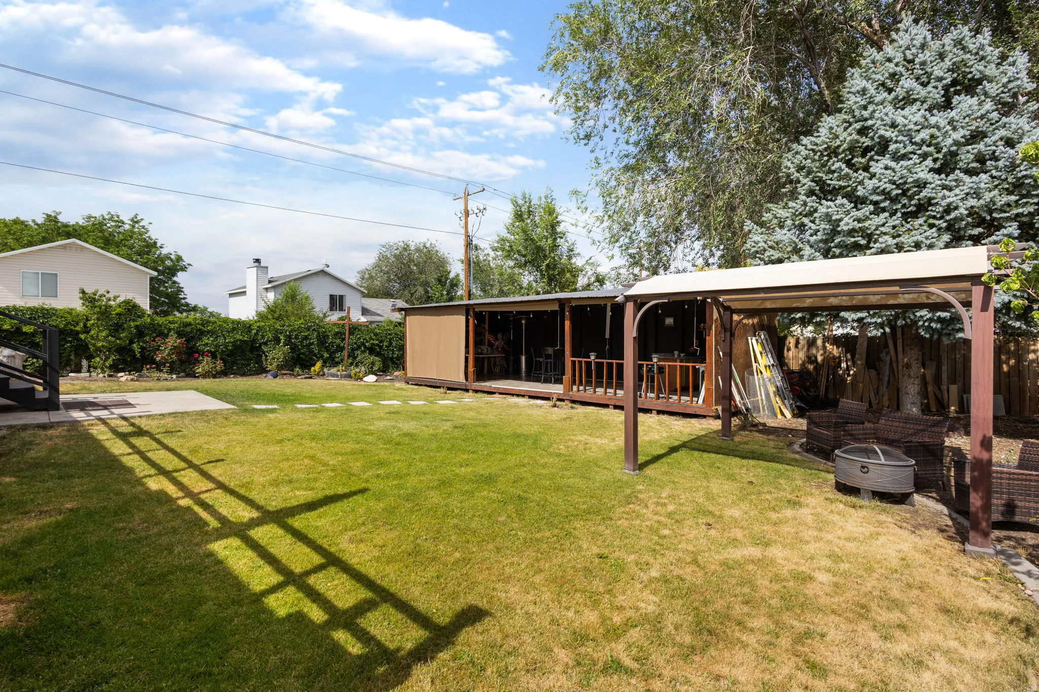 Expansive backyard featuring a large grass area, mature trees, a concrete patio, and a covered pergola with a dark wood-finish frame