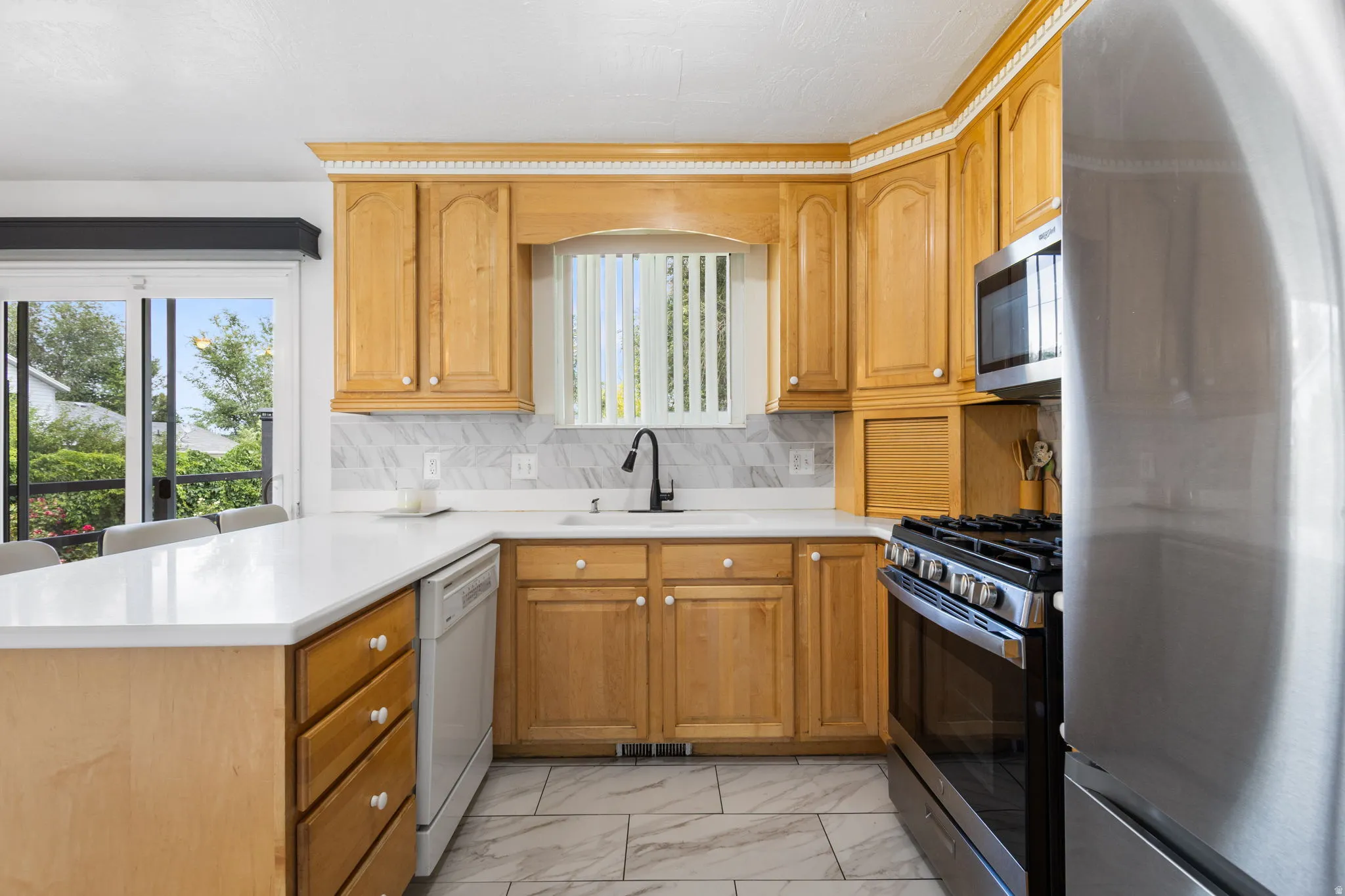 Kitchen featuring light wood cabinetry, white countertops, marble-look tile flooring, and stainless steel appliances