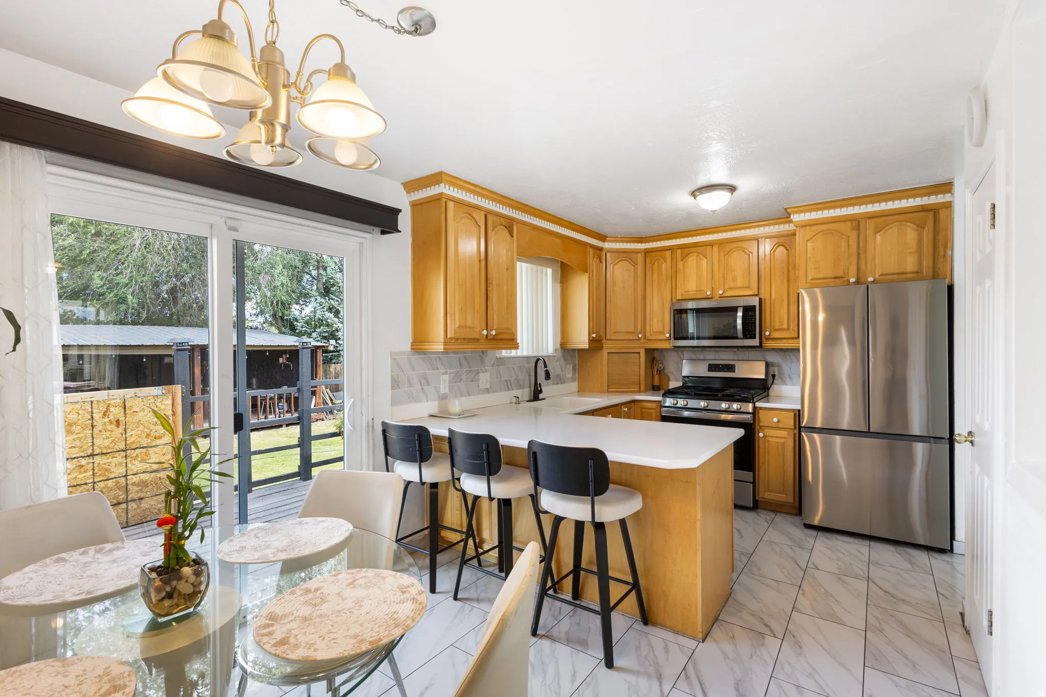 Kitchen featuring wood-finish cabinetry, stainless steel appliances, white countertops, a tiled backsplash, and light-toned floor tiling