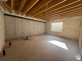 Unfinished basement offering exposed wood ceiling joists, concrete foundation walls, a window opening, and pre-plumbed floor drains