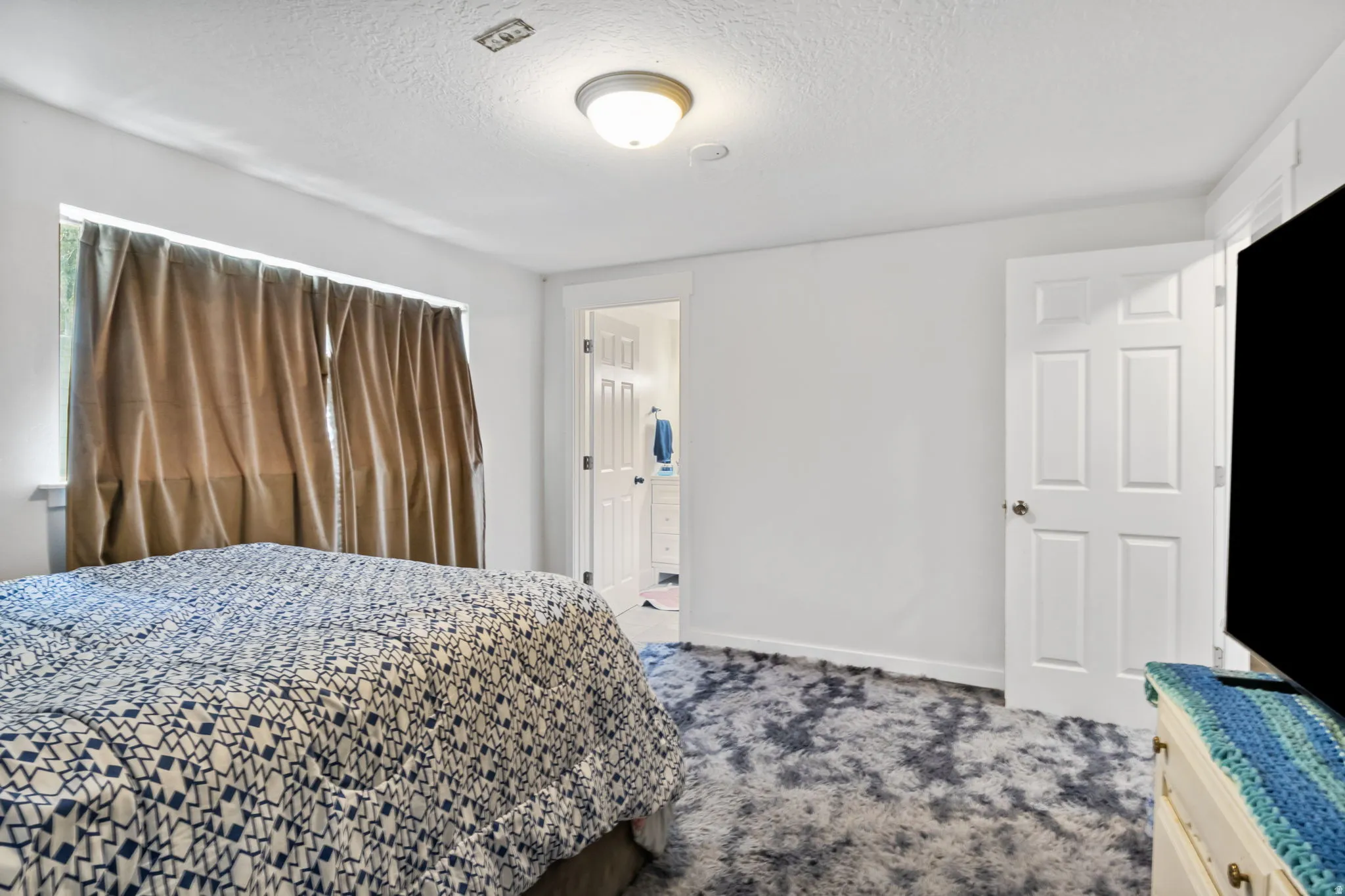 Spacious room with plush gray and white patterned carpeting, white walls, and a large window