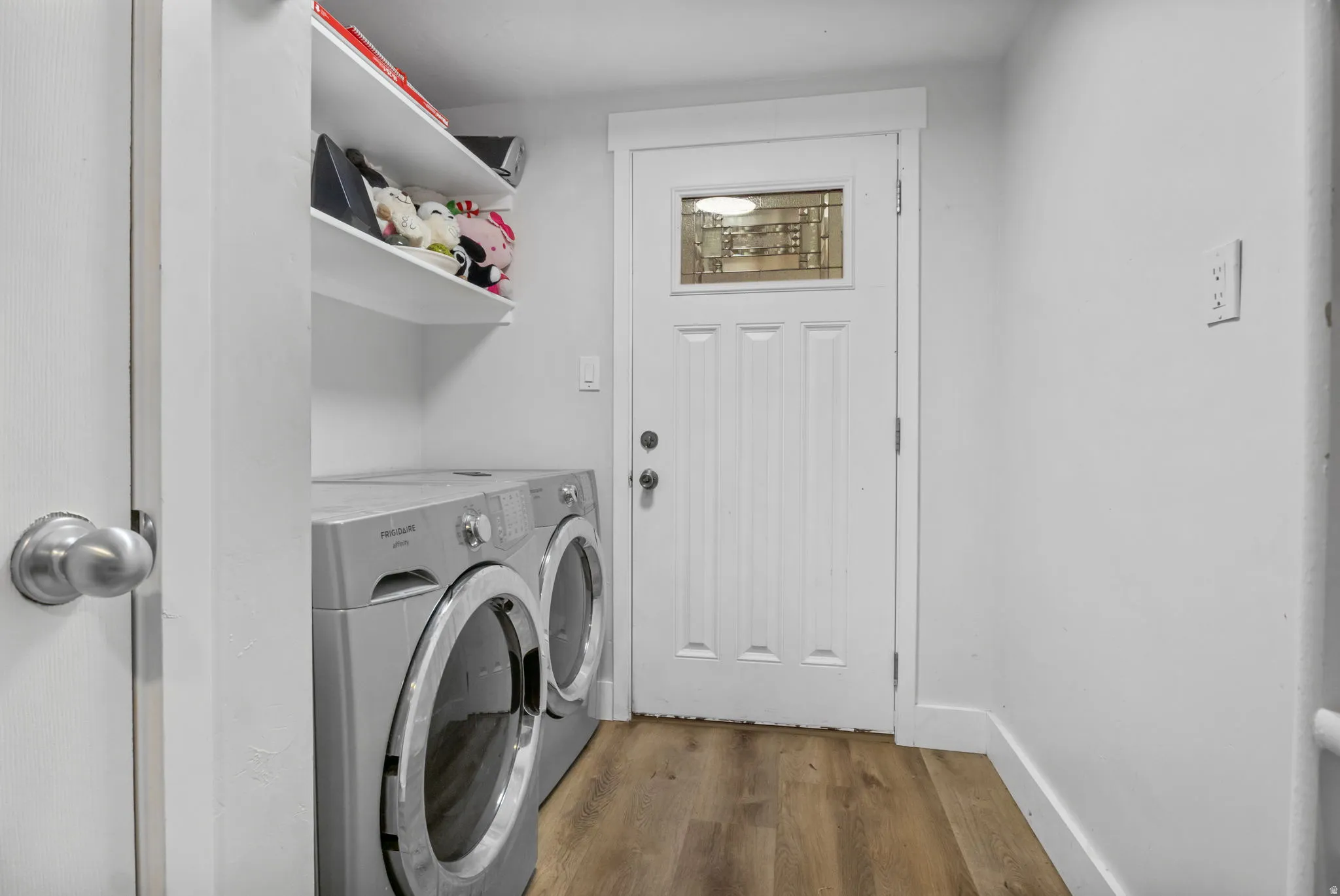 Dedicated laundry space featuring wood-finish flooring and a white paneled door with an upper glass insert