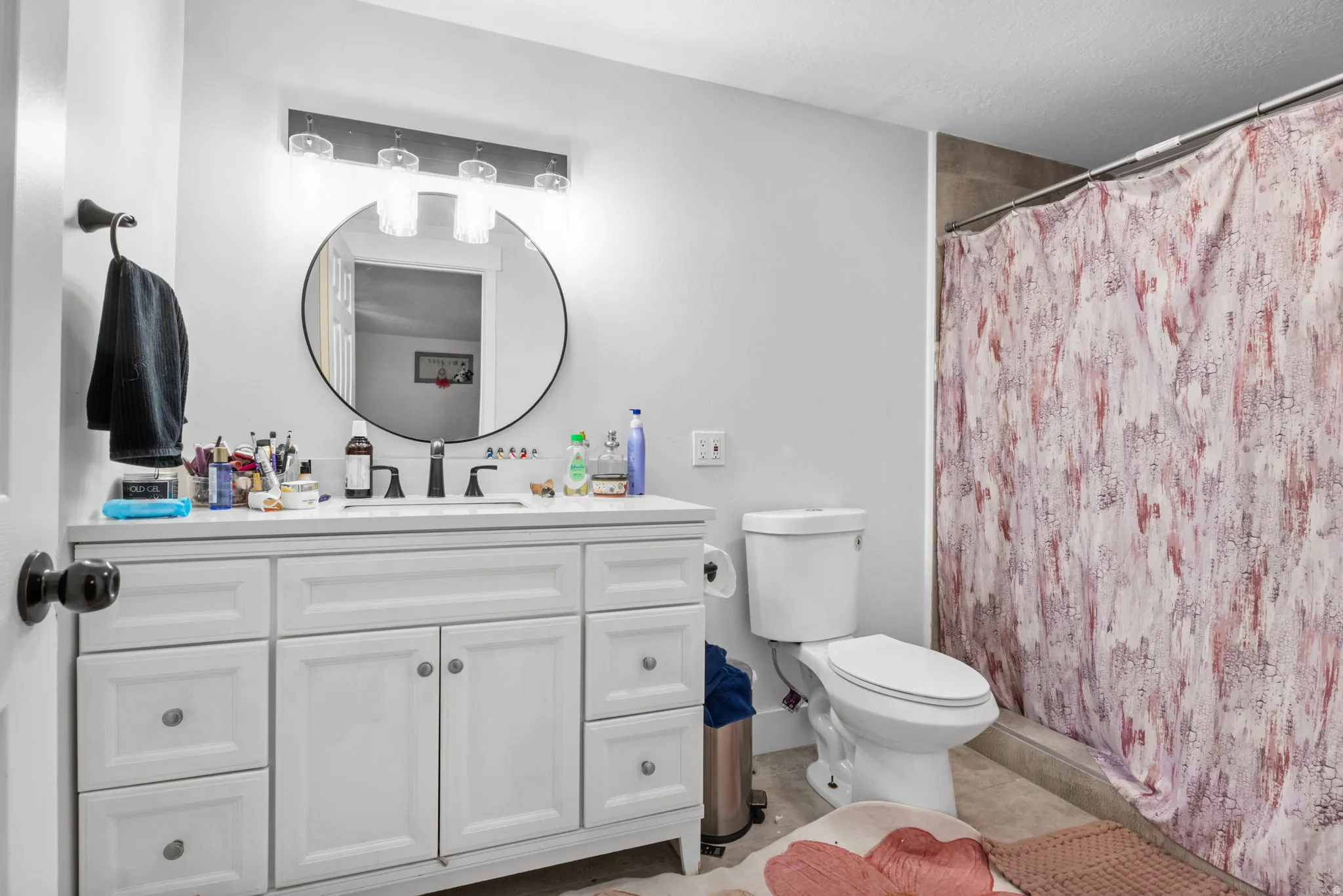 Bathroom featuring a white vanity with integrated sink, a circular mirror, and a three-light fixture