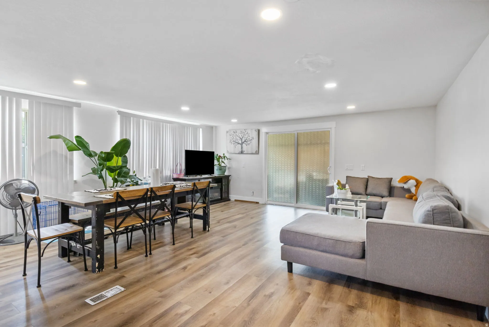 Open-concept living space featuring wood-finish flooring, recessed lighting, and white vertical blinds
