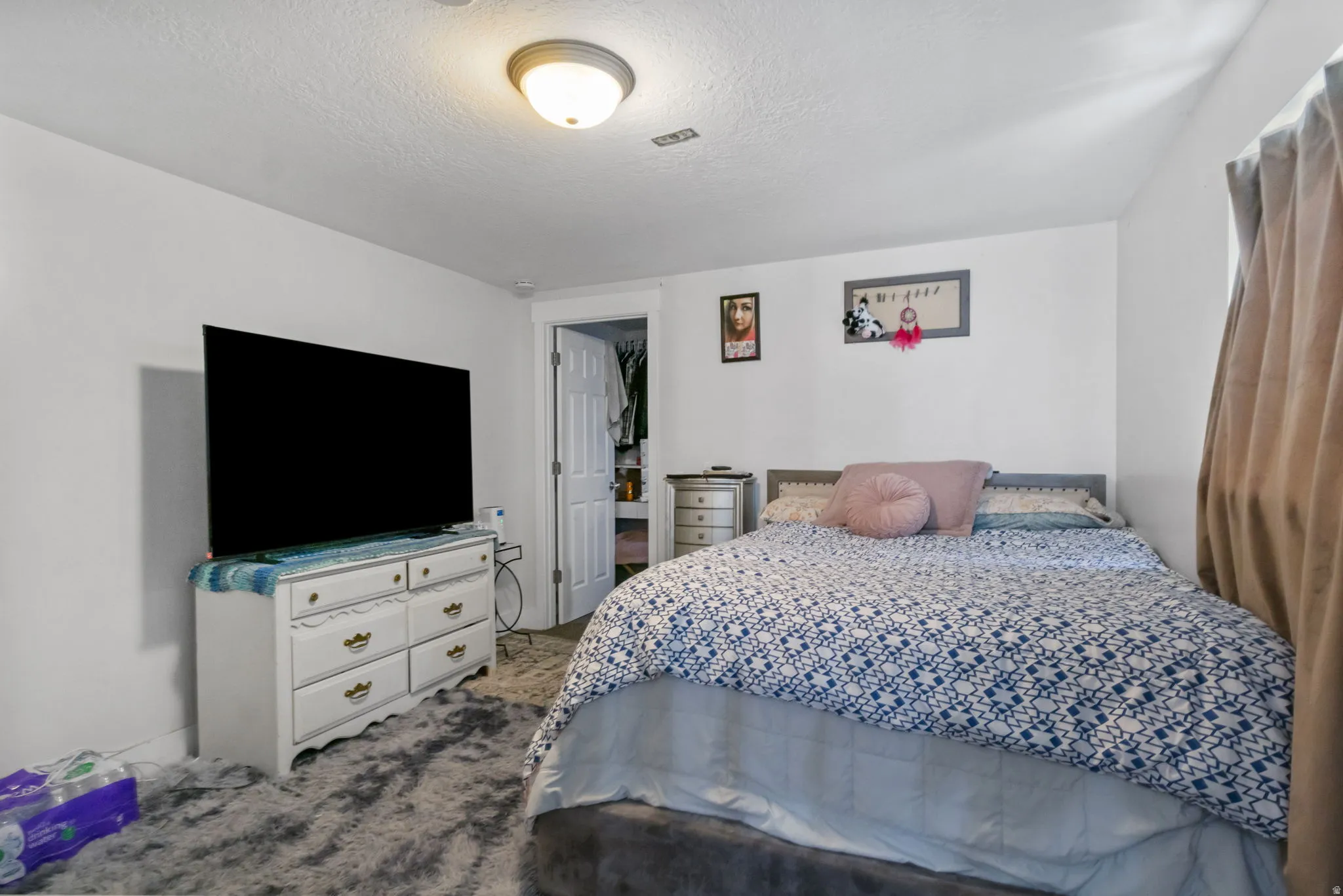 Bedroom featuring a neutral color palette, ceiling-mounted light fixture, white walls, and a visible closet entry with a white paneled door