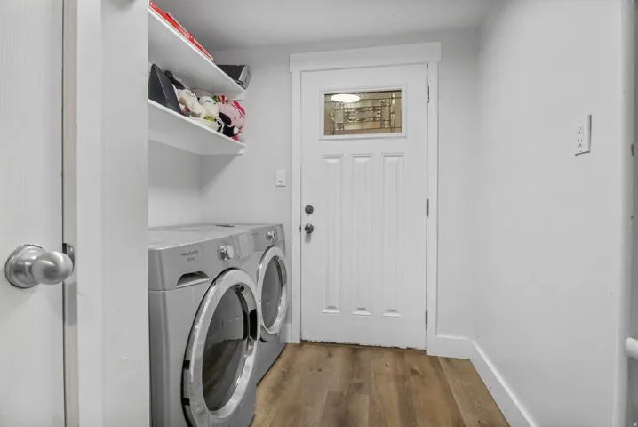 Dedicated laundry space featuring wood-finish flooring and a white paneled door with an upper glass insert