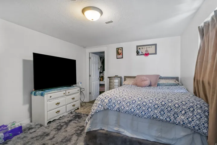 Bedroom featuring a neutral color palette, ceiling-mounted light fixture, white walls, and a visible closet entry with a white paneled door