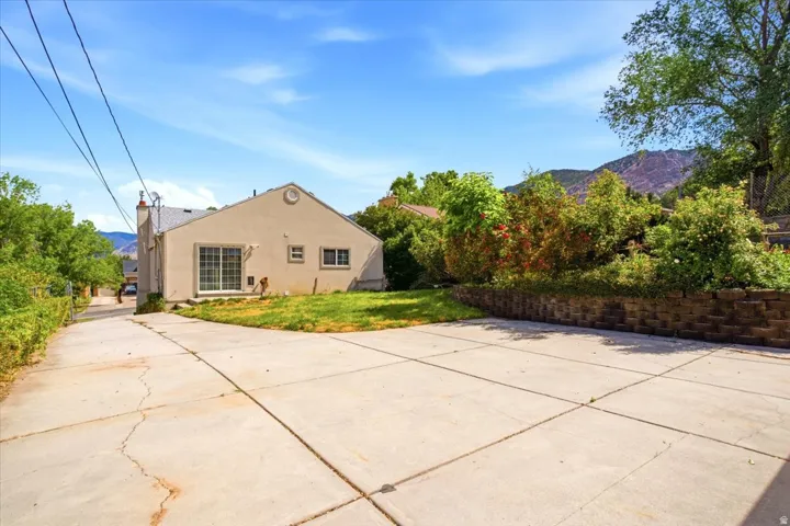 Expansive concrete driveway with a retaining wall, mature landscaping, and mountain backdrop