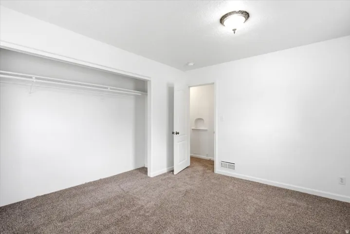 Carpeted interior room featuring a white door, overhead ceiling light fixture, white walls, and a closet with wire shelving