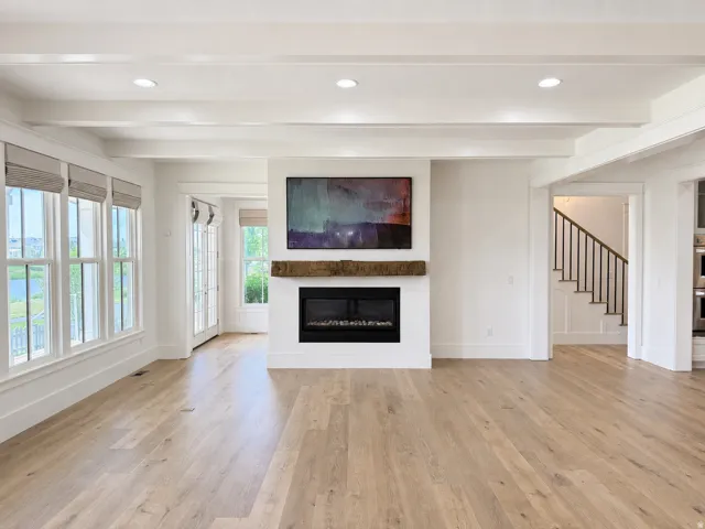 Large gathering area with engineered wood flooring, Venetian plaster fireplace with a rustic wood mantle and ceiling beams
