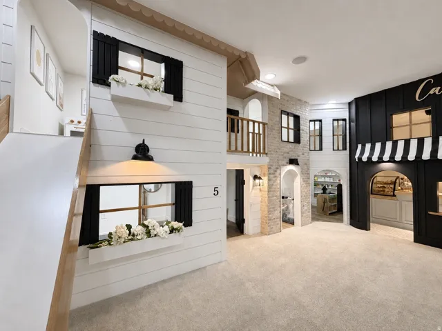 5 Pretend City Lane, a custom-built interior play structure featuring varied facades, decorative window boxes, wall-mounted light fixtures, an upper-level balcony and functioning slide