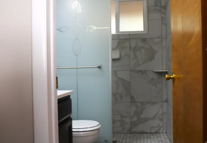 Bathroom featuring a toilet, dark wood-finish vanity with a white countertop, and a shower with white marble-patterned tile walls and hexagonal floor tiles
