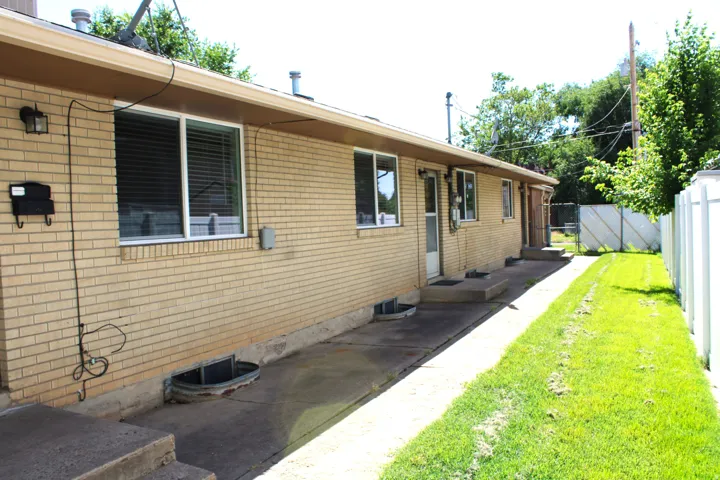 Brick exterior featuring multiple windows, a concrete walkway, and a manicured lawn