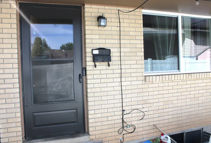 Brick exterior with a dark-paneled storm door, wall-mounted exterior light fixture.